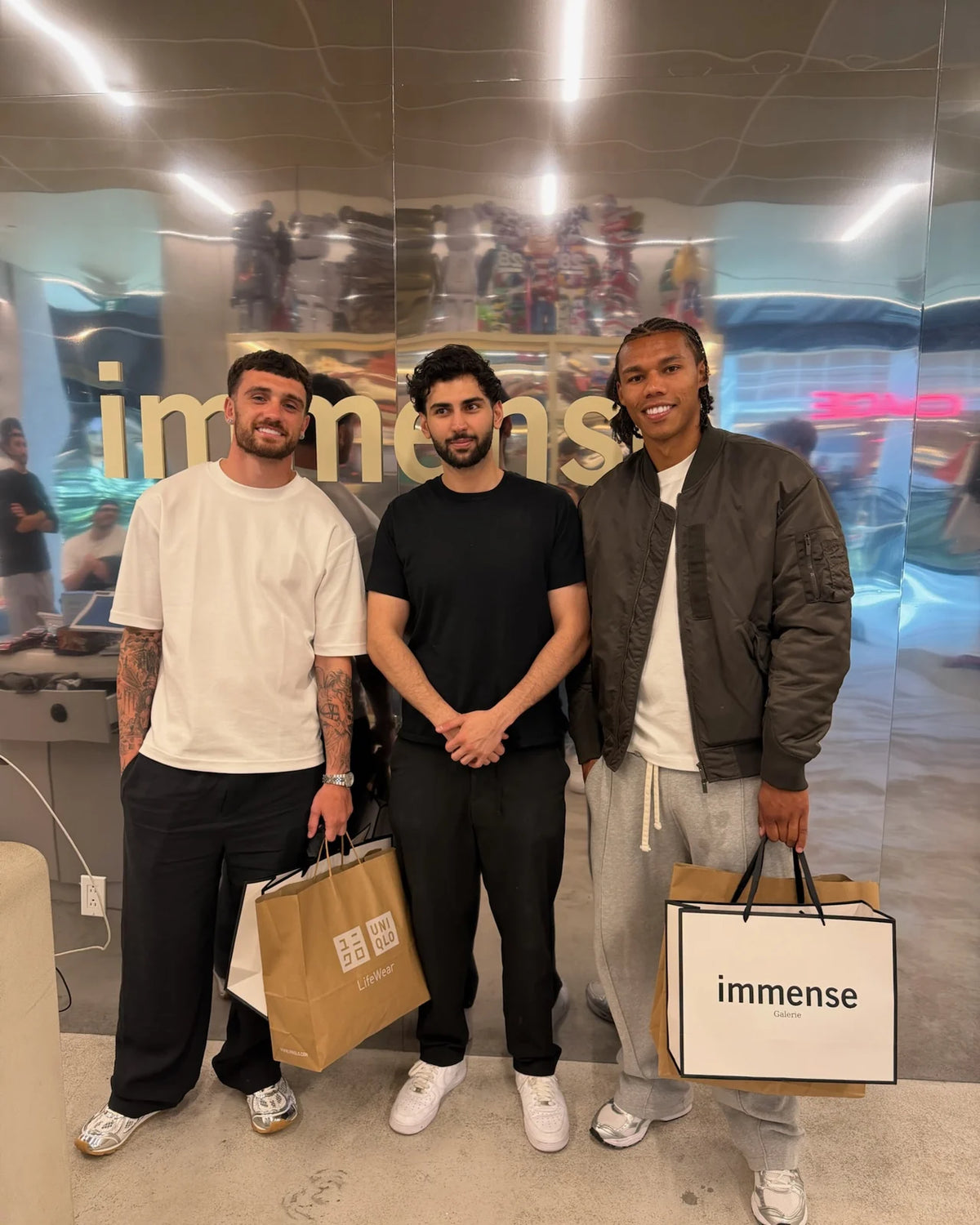 Three customers with shopping bags in front of the mirrored Immense logo wall