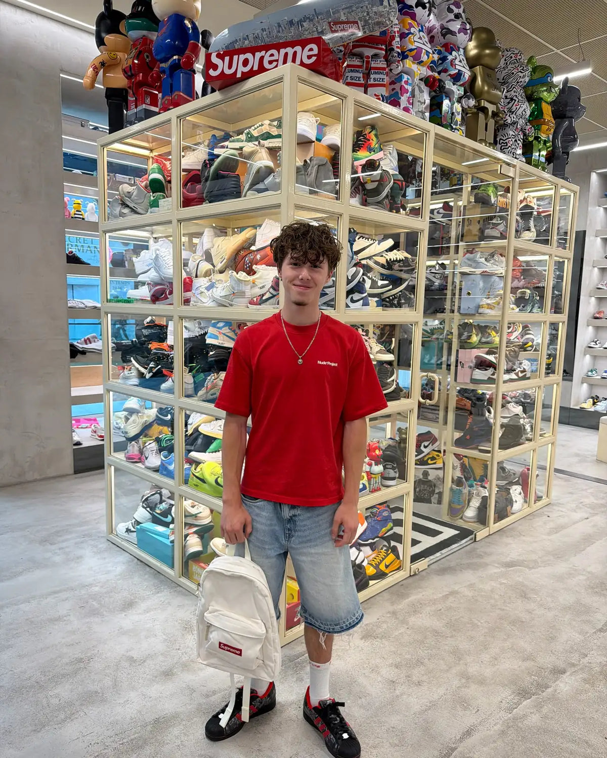 Customer with a white Supreme backpack beside the sneaker display case at Immense Galerie