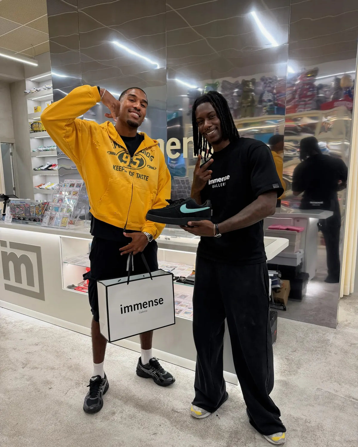 Two customers holding a Nike Air Force 1 and an Immense Galerie shopping bag